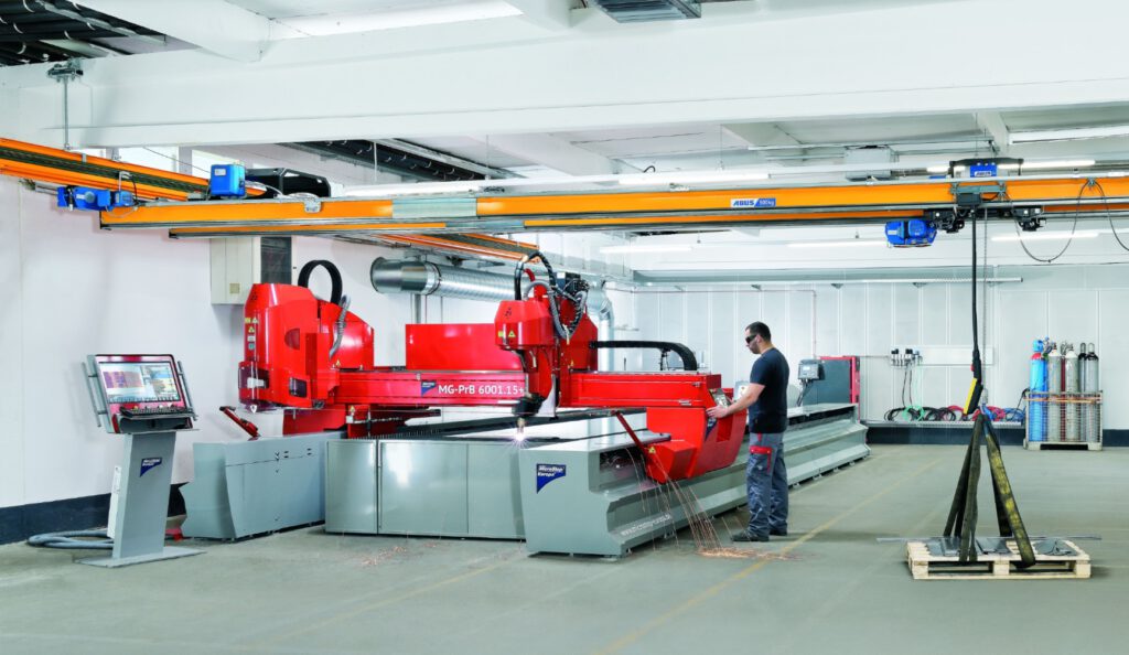 Mitarbeiter mit Schutzkleidung arbeitet an einer rot-silbernen, modernen Maschine in einer großen Industriehalle.