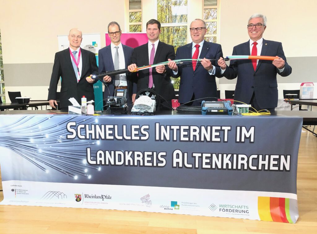 Man sieht fünf Herren im Anzug, die gemeinsam ein Glasafserkabel halten. Vor den Personen ist ein Plakat mit der Aufschrift "Schnelles Internet im Landkreis Altenkirchen" zu erkennen.