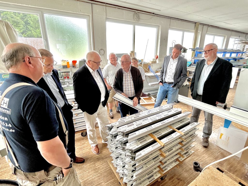 Besuchergruppe zusammen mit Firmeninhabern an einer Maschine in der Schreinerei.